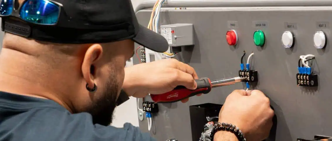 A person working on a control panel, using a screwdriver to connect wires