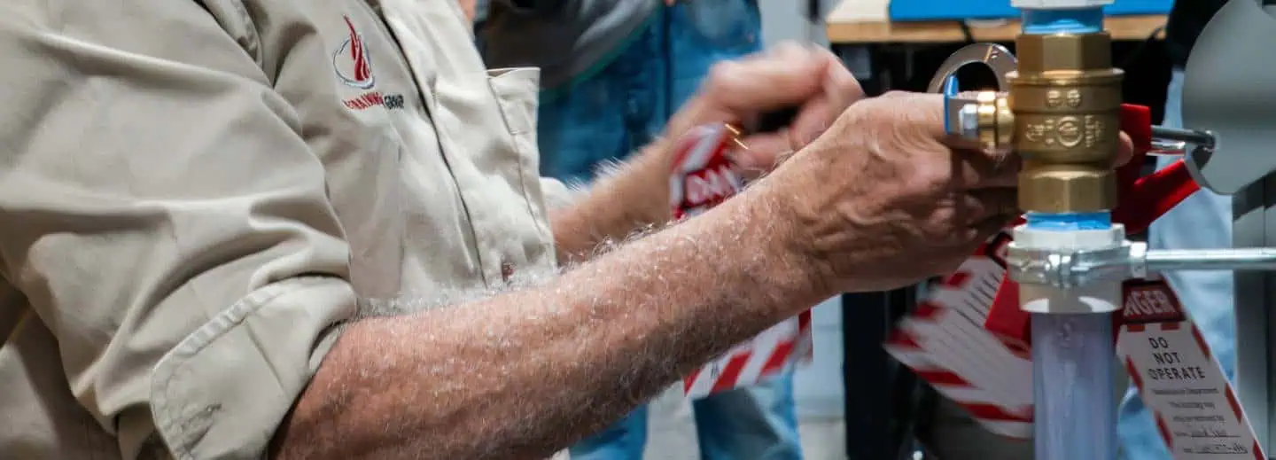 A person's hands working with plumbing equipment, including a brass valve and red tape.