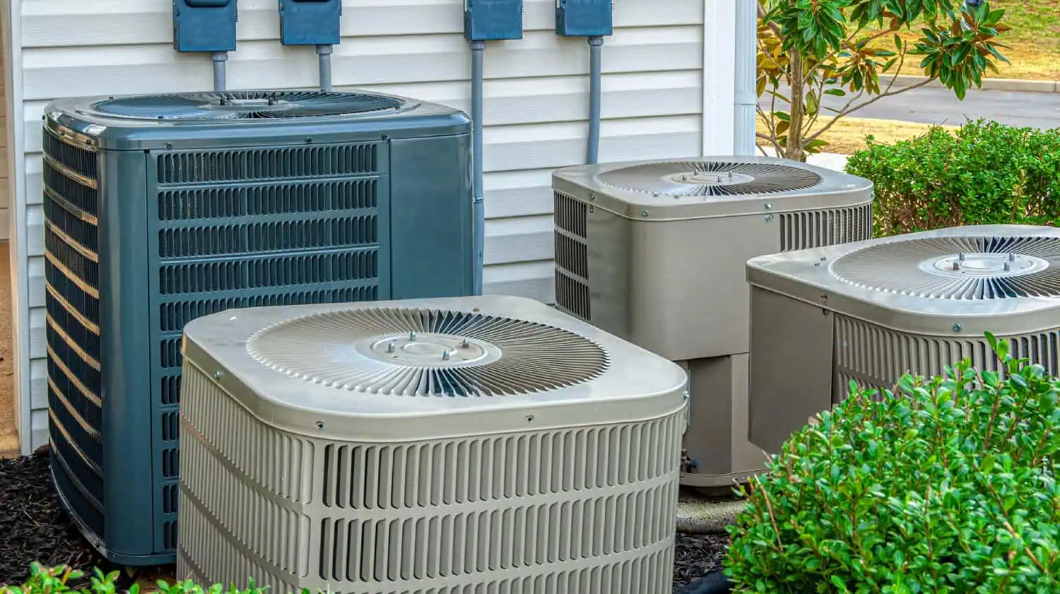 Air conditioning units placed outside a building, surrounded by greenery.