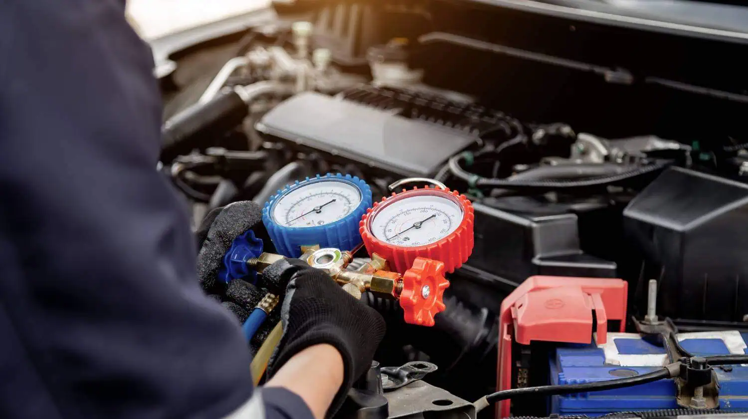 Gloved technician using pressure gauges on a car engine for HVAC service.