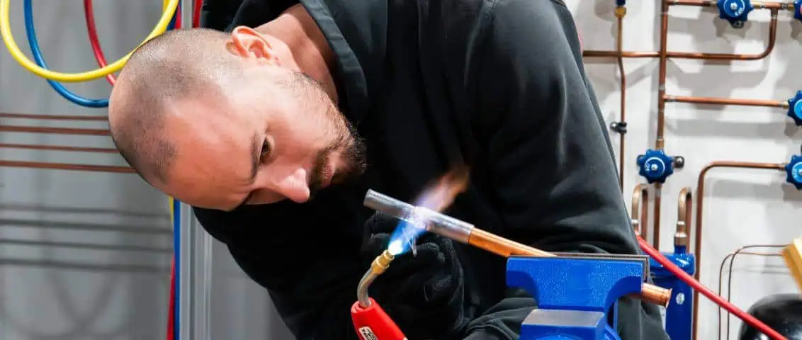 Person using a welding torch on a metal tube in an industrial setting