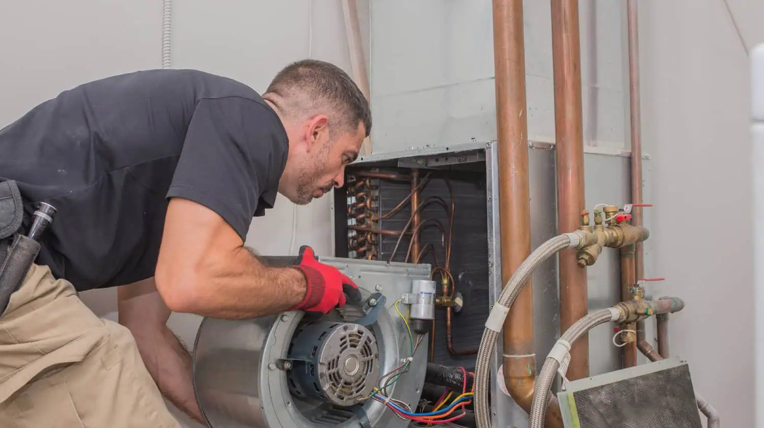 Technician repairing a motor in a mechanical room with pipes and wiring
