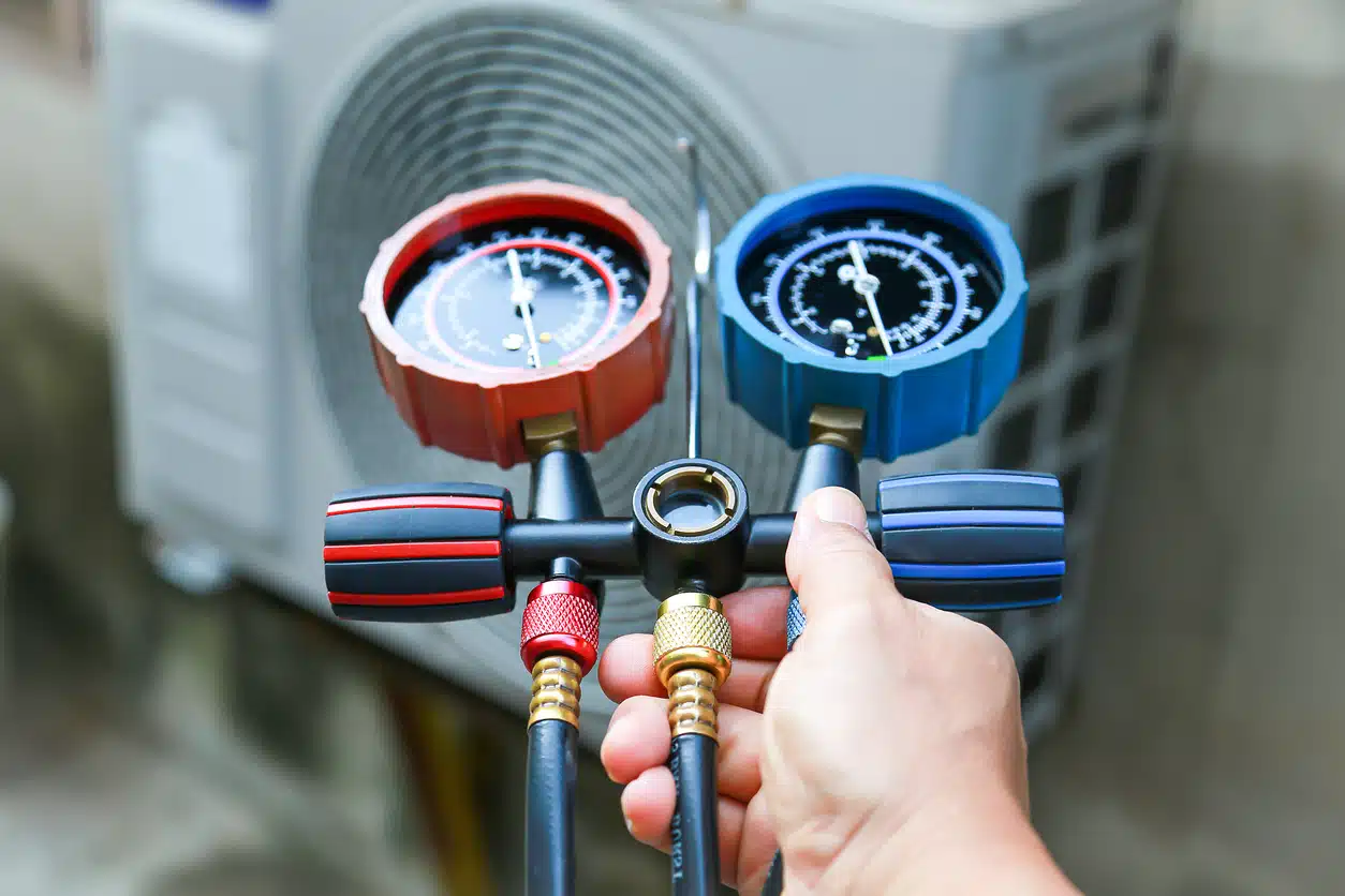 Technician holding pressure gauges connected to an air conditioning unit with colored hoses